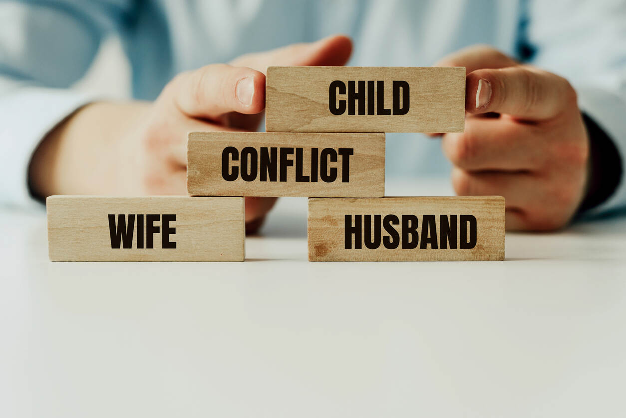 Wooden blocks with 'CHILD', 'CONFLICT', 'WIFE', 'HUSBAND' being arranged by hands, symbolizing family law mediation.
