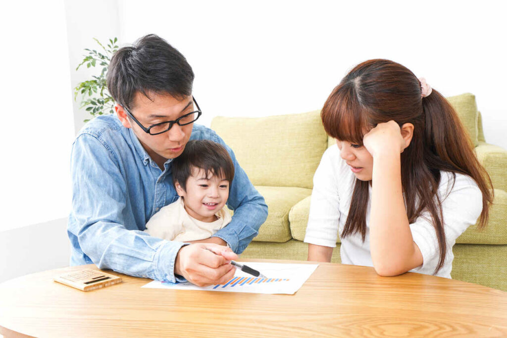 A father, mother, and child sitting at a table, with the father pointing at a graph on paper while the mother looks concerned.